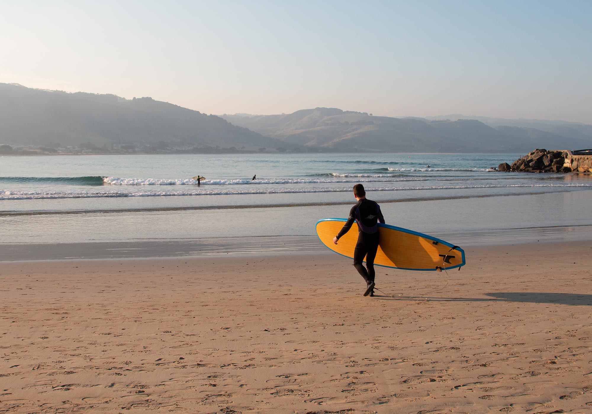 A man is walking towards the ocean holding a SUP board. 