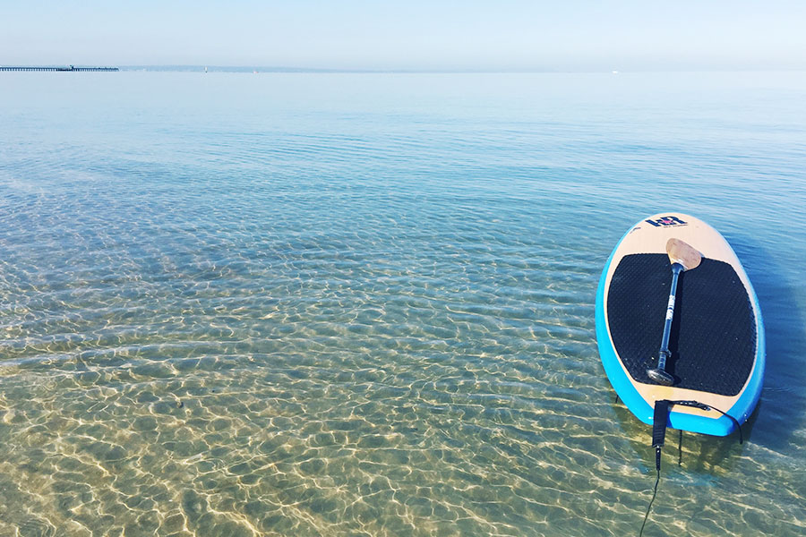 A SUP board is sitting on a flat body of clear ocean water. 