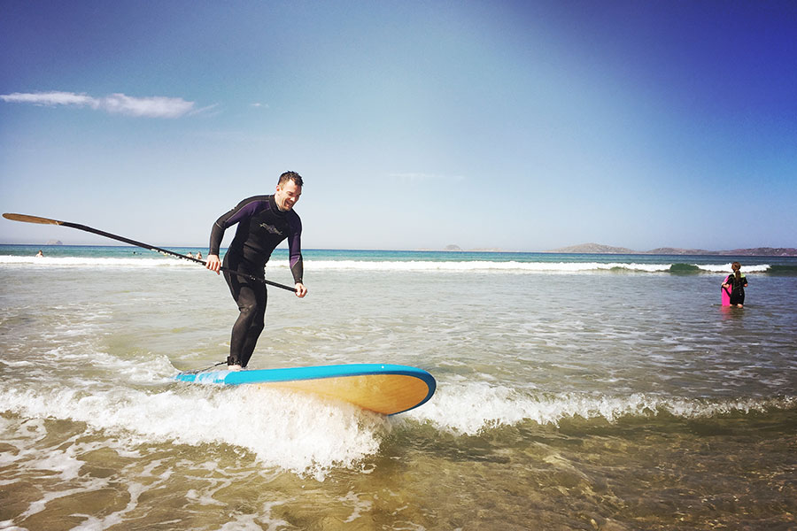 A man is SUP-ing in the shallows of a beach. 