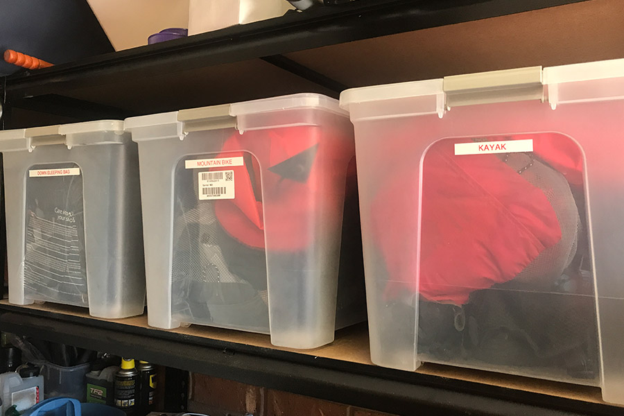 Clear storage tubs filled with camp gear, stacked on a shelf.