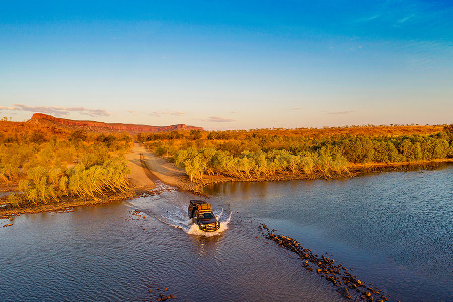 A 4WD travelling through a shallow body of water at sunset. 