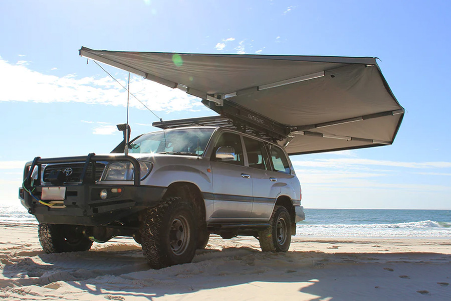A 4WD on a beach with the Supa Peg Outbound Shield 6 Freestanding awning expanded.