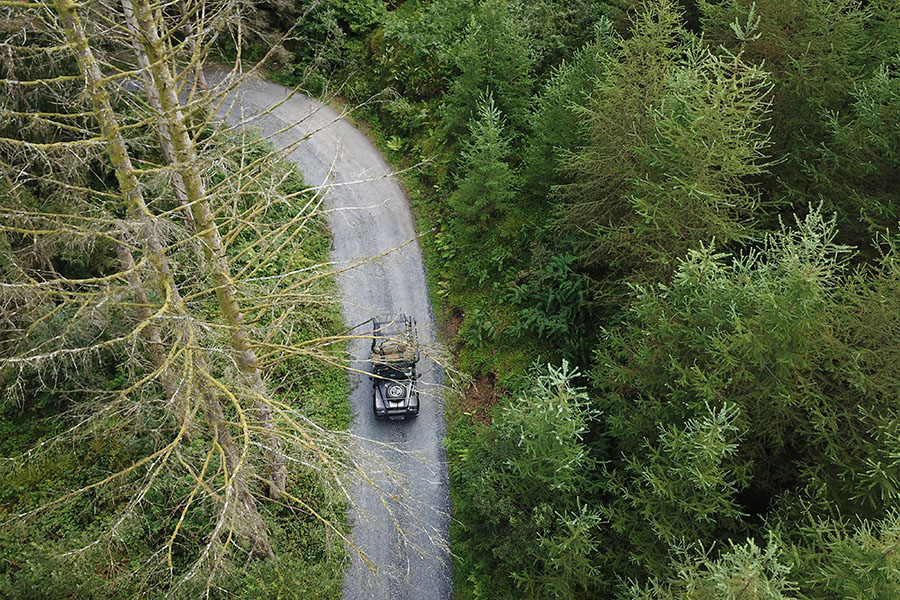 A bird's-eye-view of a 4WD on a track lined by green forest. 