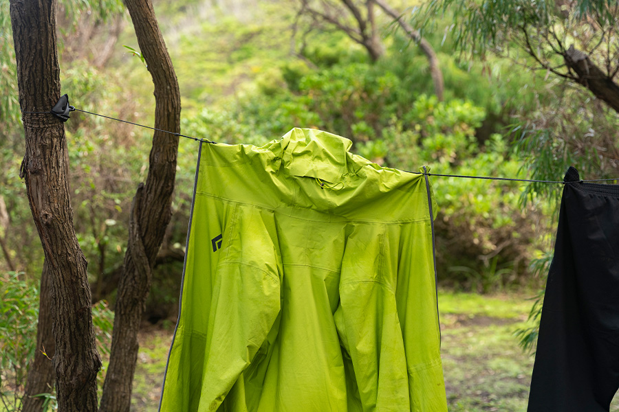 A green coat hanging on a Sea to Summit pegless clothesline between trees. 