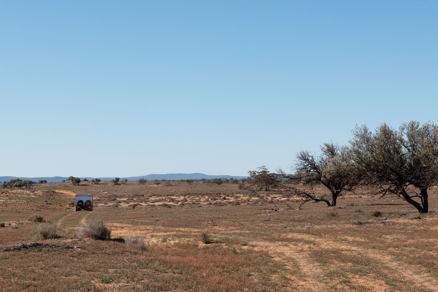 A vehicle driving off into the distance in the middle of the outback.
