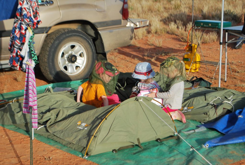Three young kids playing games on their swags. 