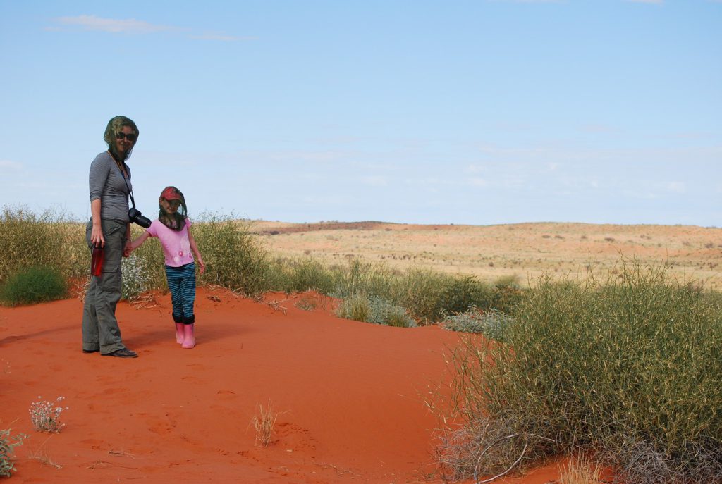A woman and her daughter in flynets, standing on red dirt. 
