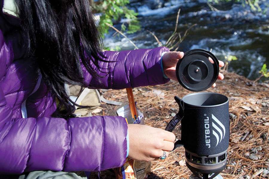 A woman in a purple jacket lifts the lid of a JetBoil Zip.