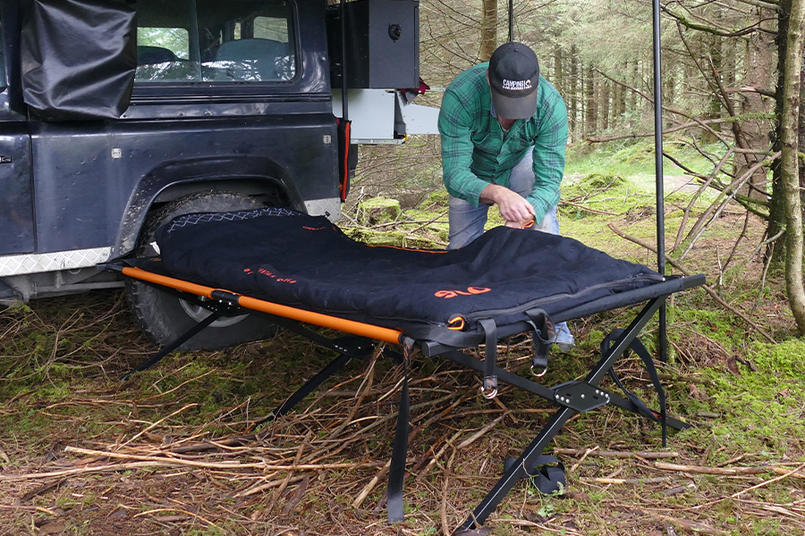 Is the infamous centre bar a deal-breaker, back breaker, or just a minor inconvenience? A man setting up a camp stretcher and sleeping bag at a campsite.