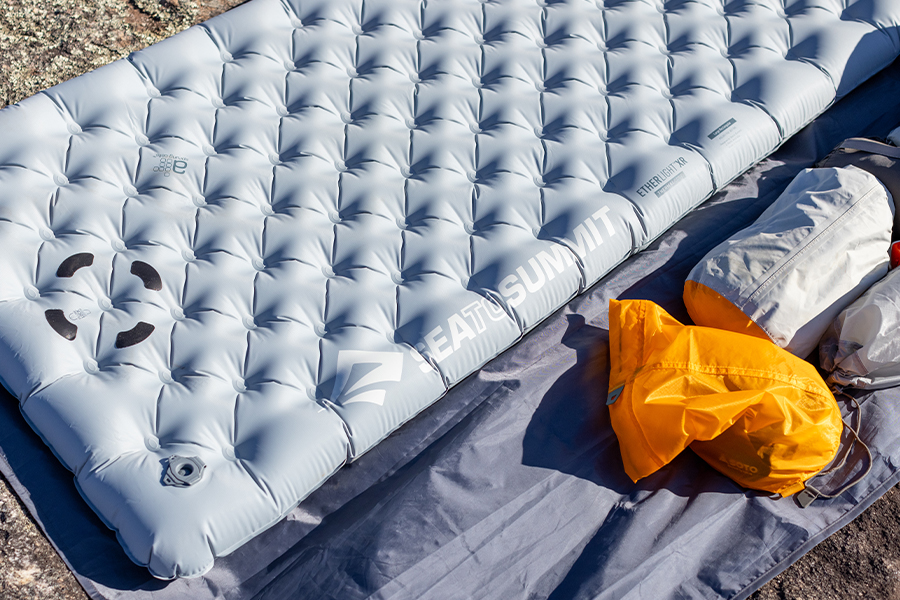 In this episode, Ben and Lauren unpack the proper storage techniques for self-inflating sleeping mats A Sea to Summit sleeping mat on a slab of rock, with the yellow stuff-sack to the side.