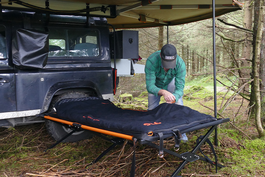 A man bending over his bedroll setup beneath an awning. 