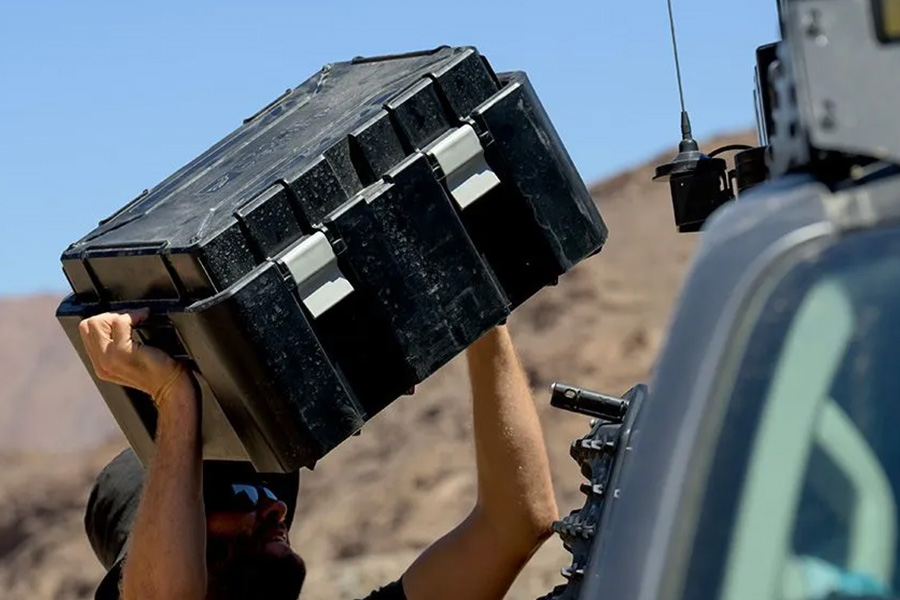 A camper lifting a box onto the top of his 4WD, which has a roof rack system.