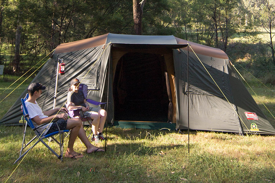 Two campers sitting outside a Coleman tent in the bush. 