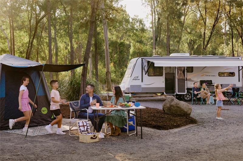 A group of campers sitting around their campsite with a camper van and tent. 