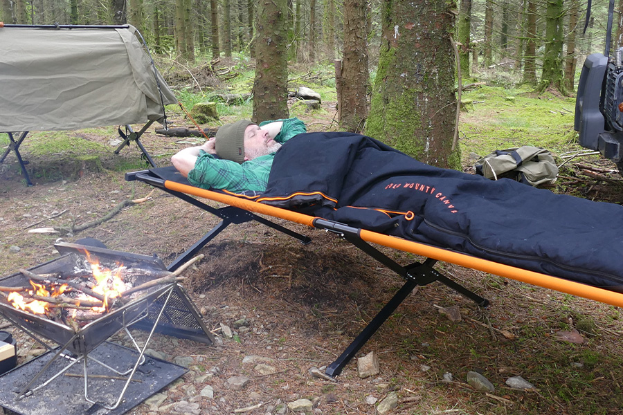 Picture of man sleeping comfortably in a sleeping bag in the open on a stretcher.
